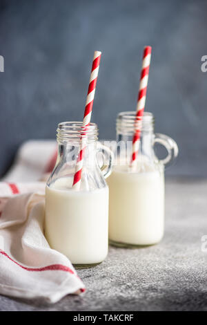 Milk in vintage bottles with stripped red and white straws on grey concrete  table with copyspace Stock Photo