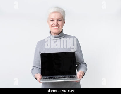 Portrait of a cheerful mature woman showing blank screen laptop computer isolated over white background Stock Photo
