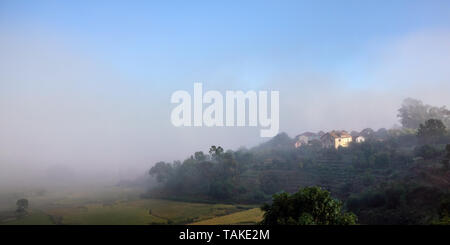 Morning fog over rice fields, sun shines through to small clay buildings - typical landscape in Alakamisy region of Madagascar Stock Photo