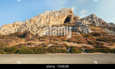 Evening sun shines on typical landscape at Karpass region of Northern Cyprus, small rocky formations by asphalt road Stock Photo