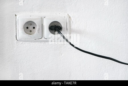 Rough facade white wall with two european style power outlet, one socket plugged black cable Stock Photo