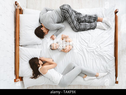 Funny family with one newborn child in the middle of bed