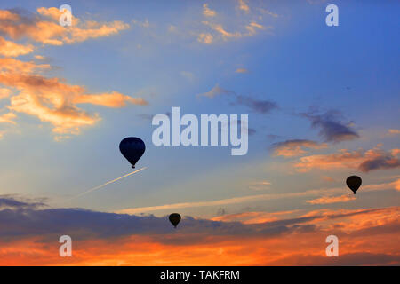 Silhouettes of balloons raising tourists into the blue sky above the fiery red clouds in the early morning against the backdrop of an airplane flying  Stock Photo