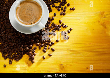 Delicious cup of frothy cappuccino coffee on scattered roasted coffee beans in the corner on colorful yellow wood with copy space Stock Photo