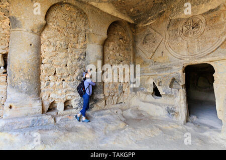 Young beautiful girl sights in the pillared hall of an old, antique, underground church carved out of sandstone rock in Cappadocia Stock Photo