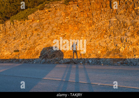 A traveller playing with his shadow at sunrise along the road. Shadow of a person casted on a golden rock wall. Stock Photo