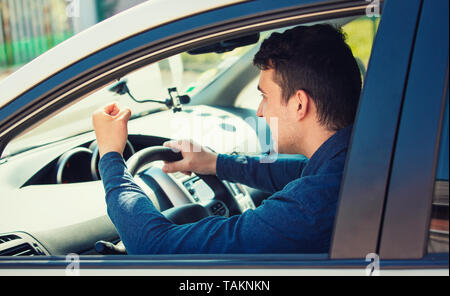 Young man driver yelling and shaking his fist threatens another motorist. Annoyed and angry guy screaming and shouting in his car. Bad and aggressive  Stock Photo