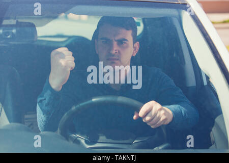 Young man driver sitting in his car behind the wheel shaking his fist threatens another motorist. Bad and aggressive behavior on road concept. Stock Photo