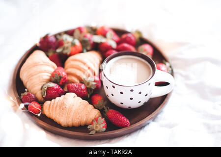 Cup of coffee with strawberry croissants on tray in bed closeup. Good morning. Stock Photo