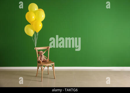 Chair with toy bear and balloons on color background Stock Photo