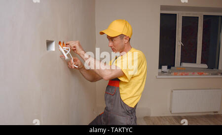 Electrician puts socket. Electrician working with wires in new apartment. Stock Photo