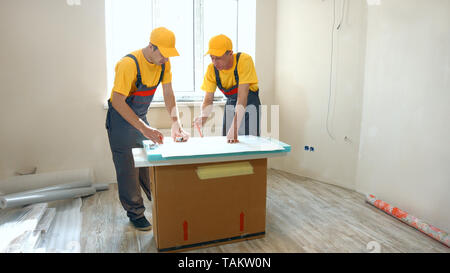 ?onfident builders looking at building plan at construction site. Two professional builders looking at plan of building indoors. Stock Photo