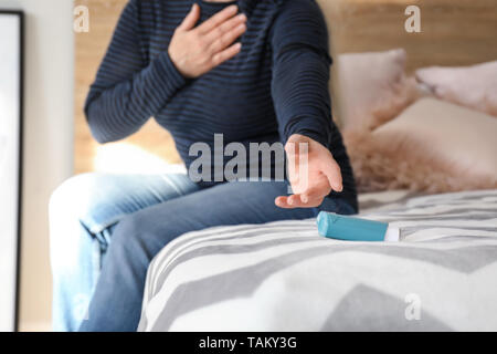Mature woman with asthma attack taking inhaler from bed Stock Photo
