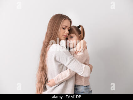 Sad woman after divorce hugging her little daughter against light background Stock Photo