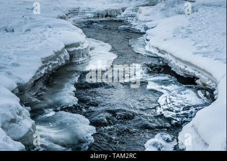 Spring thawed patch in the ice of the river. Frozen ice and snow by the river side. Natural background. Stock Photo