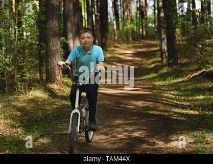 A young caucasian boy is riding bicycle on a sunny day. Boy is riding bike through countryside. Boy is riding a bicycle through the forest. Stock Photo