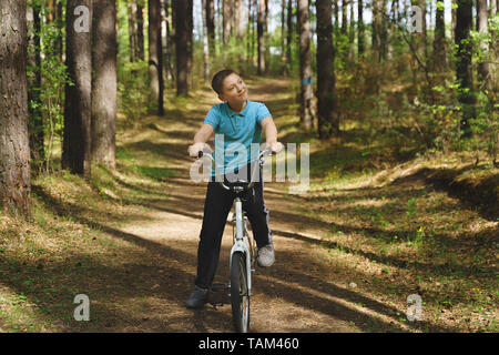 A young caucasian boy is riding bicycle on a sunny day. Boy is riding bike through countryside. Boy is riding a bicycle through the forest. Stock Photo