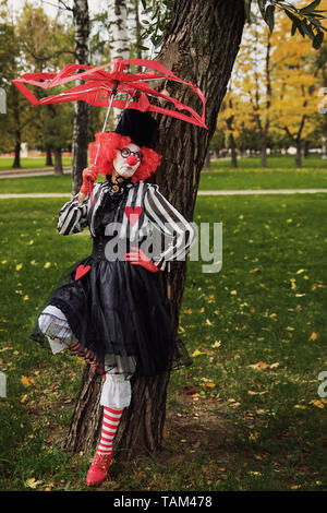 clown in red wig with an umbrella in the park Stock Photo