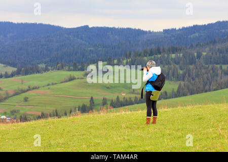 A young girl photographer shoots the landscape of the Carpathian slopes on a fresh spring morning Stock Photo
