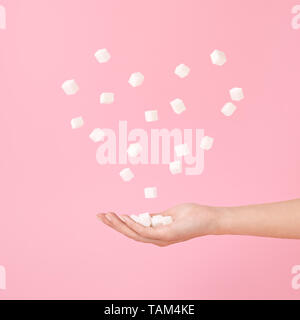 Handful of sugar cubes in hand and flying sugar in heart shape. Levitation on pastel pink. Women, mothers, valentines day Concept. Stock Photo