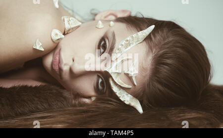 Fairy tale creature with thorns on skin lying on black fur rug. Female devil with cunning look tempting people. Girl with artistic make-up isolated on Stock Photo