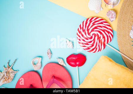 Female beach accessories on sky blue and yellow background, top view. Flat lay of sunglasses, pink flip flops, seashells , towel, straw hat, lollipops Stock Photo