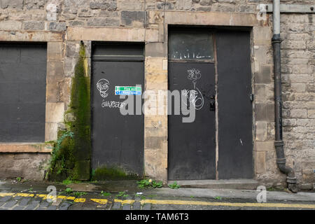 Worn old black doors (fire exit) with graffiti and damp damage from overflow, St Ninians Place, Edinburgh city centre, Scotland UK Stock Photo