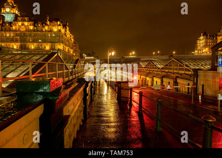 Footpath and road entrance leading underground to Waverley Railway station on a wet night, Edinburgh. The Balmoral hotel is in the background Stock Photo