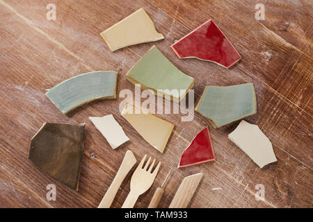 Close-up of colorful ceramic shards of broken plates and wooden sculpting tools on scratched table Stock Photo