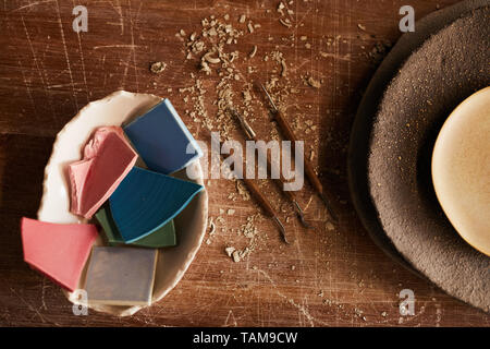 High angle view of handmade ceramics pieces in bowl, stack of textured plated and various craft tools for moulding Stock Photo