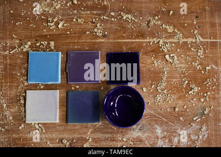 High angle view of ceramic samples in blue shadows and purple bowl placed on dirty scratched table with clay dust Stock Photo