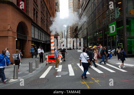Looking down John St with steam coming out of a pipe - Financial District, Manhattan - New York City Stock Photo