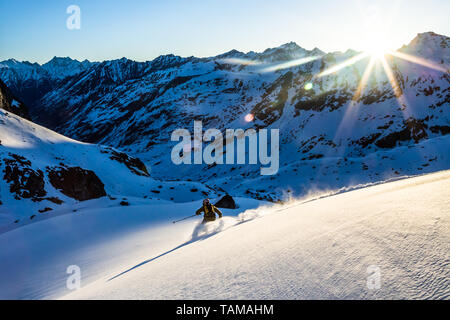 Below the Snowbird hut, a young man skis in the first light of the morning in the backcountry of the Talkeetna Mountains near Hatcher Pass in Alaska. Stock Photo
