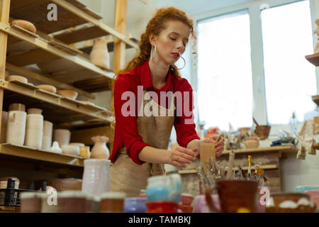Preparing paints. Focused ginger lady setting working place for painting while spending time in workshop Stock Photo