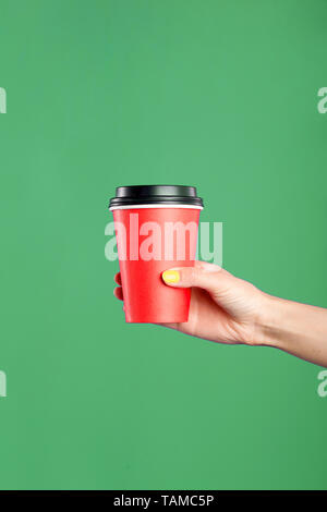 Female hand holding red takeaway paper coffee cup isolated on green background. Space for design. Beverage, breakfast concept. Vertical shot. Stock Photo