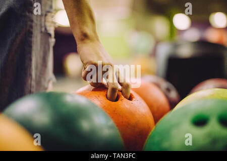 Hand choosing a bowling bowl. Close-up of female hand taking ball at bowling club. Stock Photo