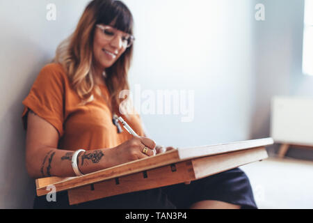 Freelancer sitting at home and writing. Close up of a creative artist making a sketch sitting on floor. Stock Photo
