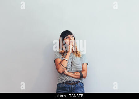 Portrait of a businesswoman standing against a wall thinking about a solution. Close up of a woman standing with hand on chin and looking away. Stock Photo