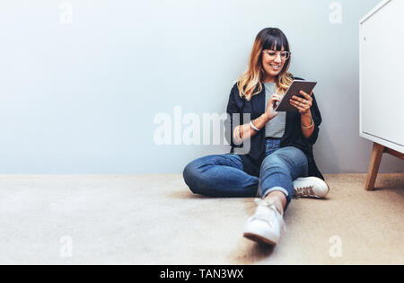 Smiling woman sitting on floor using a tablet pc. Relaxed businesswoman checking her mails on a tablet pc. Stock Photo