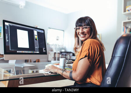 Cheerful female illustrator working on computer. Smiling artist working on digital editing on a computer at office. Stock Photo