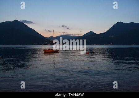 Beautiful panoramic view to the lake Como with sailing boat anchored near the Varenna port at sunset twilight in spring. Stock Photo