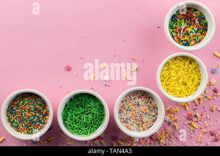 Sprinkles on pink background - Assorted colourful cake topping sprinkles in little white bowls on pink - top view Stock Photo