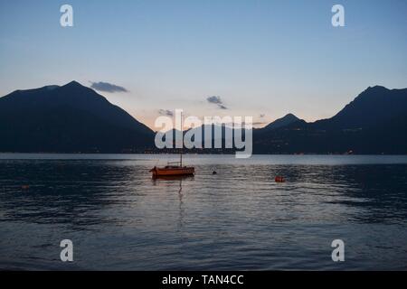 Beautiful panoramic view to the lake Como with sailing boat anchored near the Varenna port at sunset twilight in spring. Stock Photo