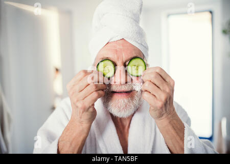 Senior man with cucumber on front of his eyes in bathroom indoors at home. Stock Photo