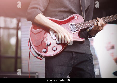 Guitarist in a gray sweater and dark jeans plays a tune on a beautiful red electric guitar on stage during a concert. Stock Photo