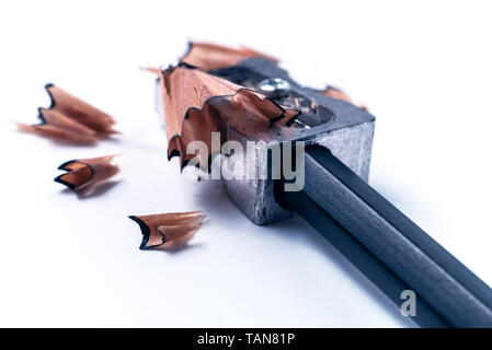 Macro closeup of sharpening a pencil with a grey metal pencil sharpener with wooden swirl shavings on white background - Concept of school education Stock Photo