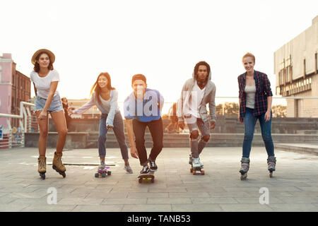 Group of diverse young people skateboarding and rolling in urban area Stock Photo