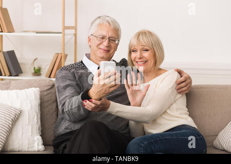 Happy Senior Couple Making Video Call And Waving To Caller Stock Photo