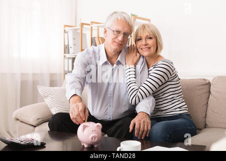 Family Budget. Senior Couple Putting Coin In Piggybank Stock Photo