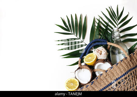 Summer still life composition with straw basket bag, lush palm leaves, lemons, coconut and glass bottle of water isolated on white background Stock Photo